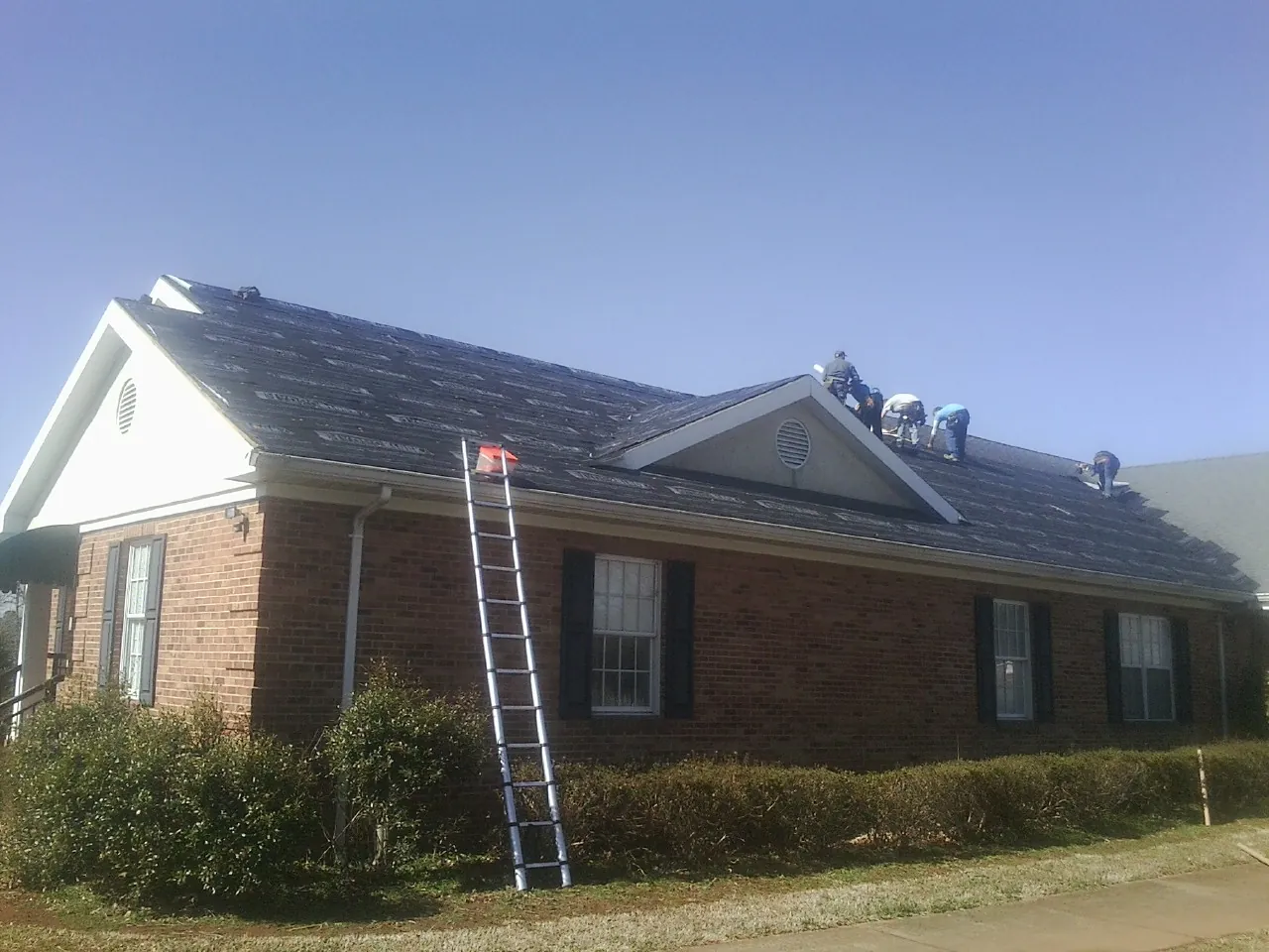 Crew tearing shingles off a brick ranch roof with a ladder set — Emergency Roof Repair work by our crew in Point Marion