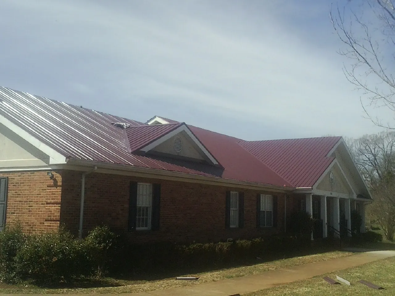 Red metal roof with gabled entries on a long brick building, from a Hail Damage Roof Repair job in Point Marion