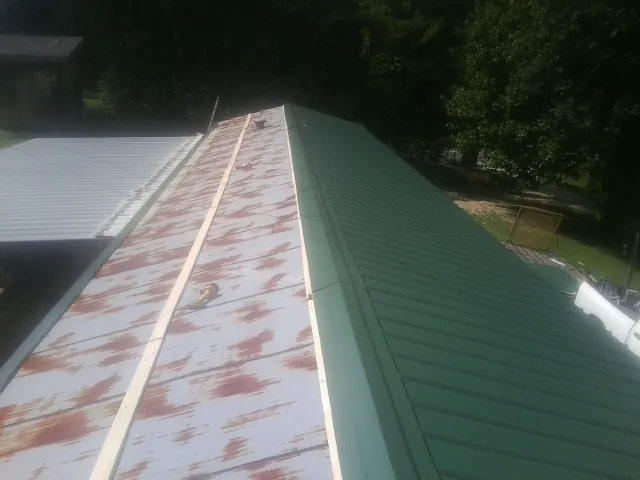 Old rusted panels beside newly installed green metal roofing — Wind Damage Roof Repair by Roofing Brothers in Point Marion