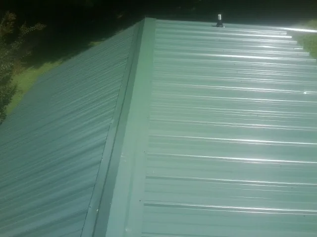 New green metal panels meeting at the ridge of a roof — Flat Roof Repair work by our crew in Point Marion