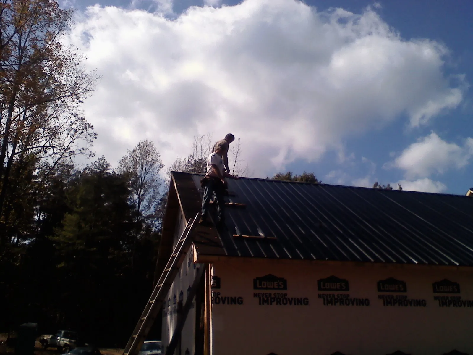 Roofer fastening dark metal panels high against a cloudy sky, from a Roof Inspection job in Point Marion