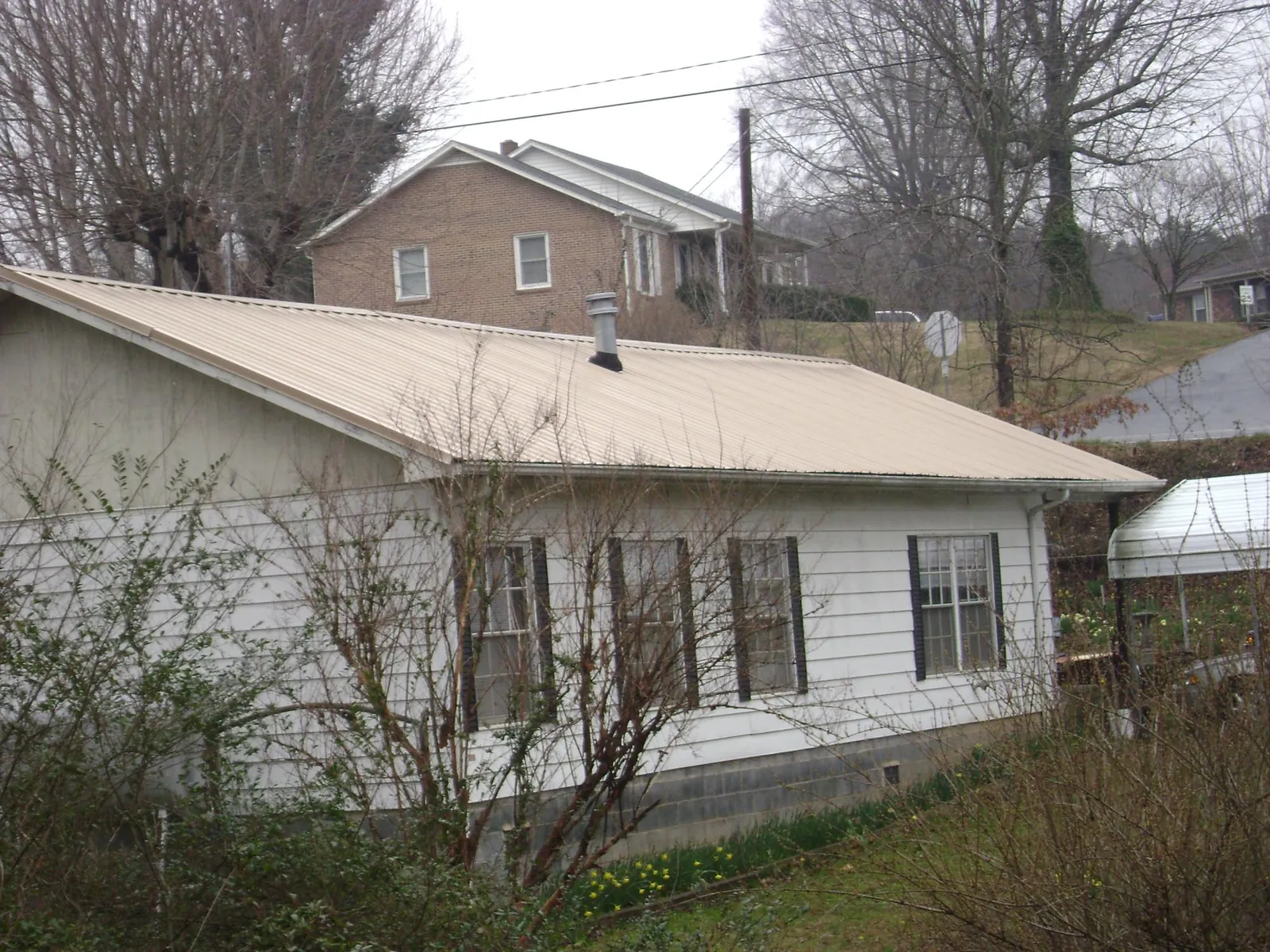 Tan metal roof on a white sided house set into a hillside — Commercial Roofing by Roofing Brothers in Point Marion