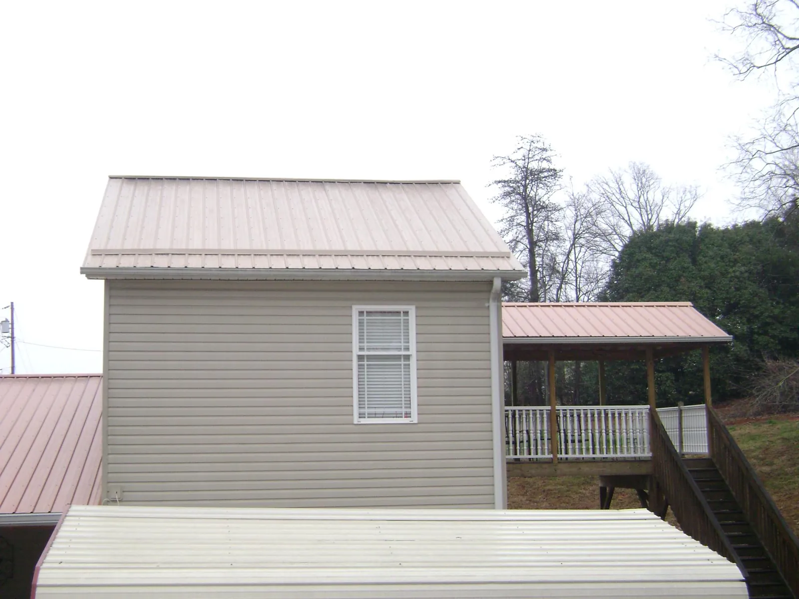 Tan metal roofs on a two story addition and attached porch, from a Roof Replacement job in Point Marion